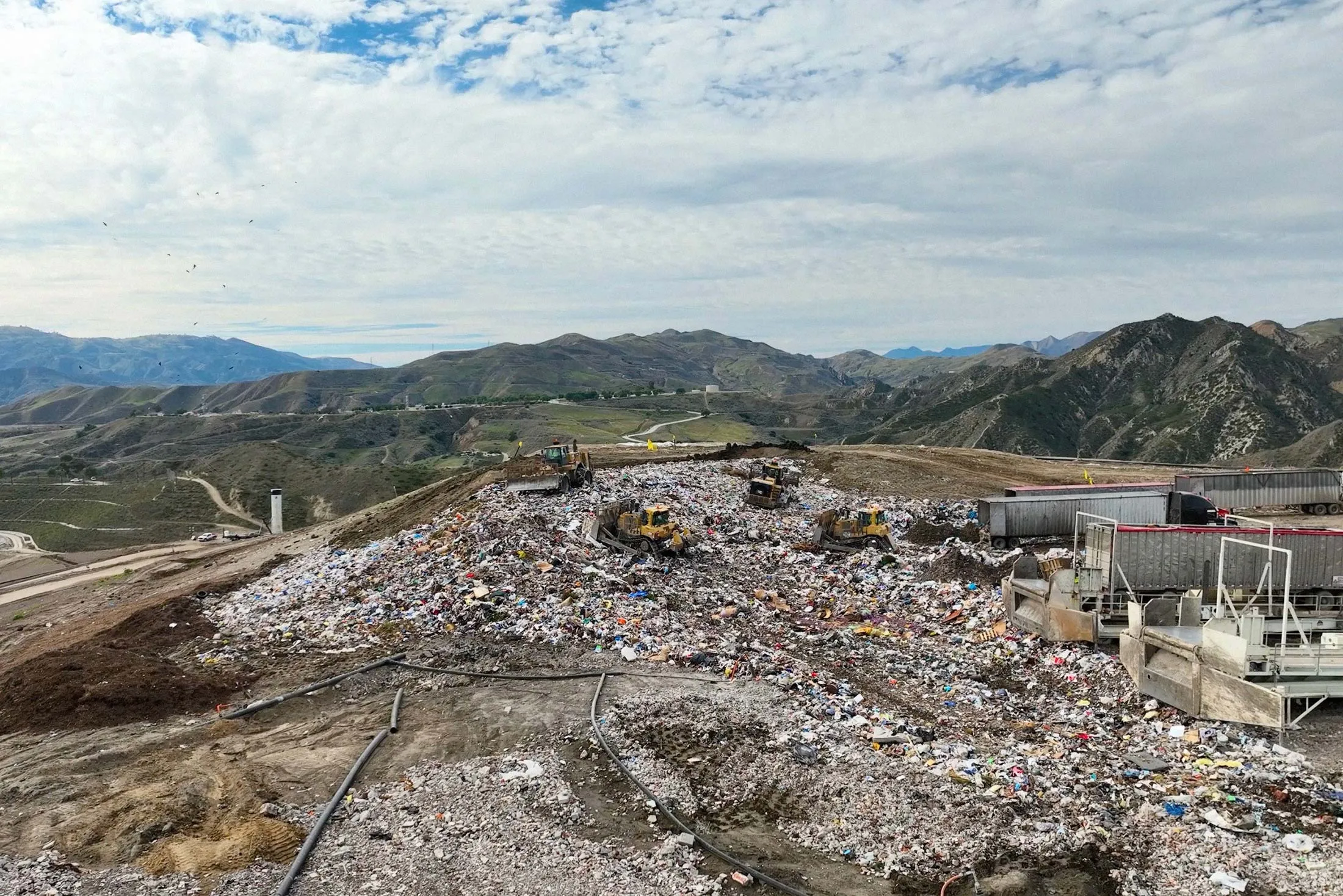 Aerial view of a landfill working face with heavy equipment operating in geofenced hazard zones — Tango uses RTK GPS to mark and protect them
